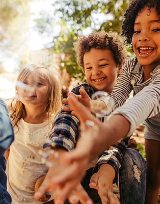 Group of kids playing with soap bubbles in forest. Boy blowing soap bubbles with friends trying to catch the bubbles.